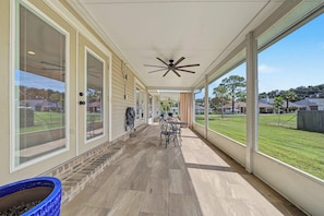 Un patio cubierto con ventilador de techo, mobiliario exterior y vistas a un barrio residencial.