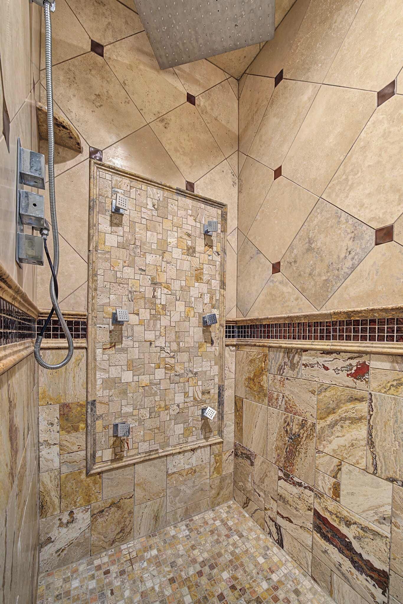 Una ducha con pared y suelo de azulejos, un cabezal de ducha de mano y una manguera.