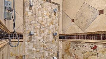 Una ducha con pared y suelo de azulejos, un cabezal de ducha de mano y una manguera.
