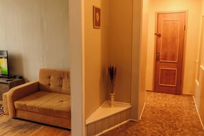 A living room with a sofa, a television, and a small table with a vase. - Old Town Riverside Apartment, Retro Vibe & River Panorama (Vilnius)