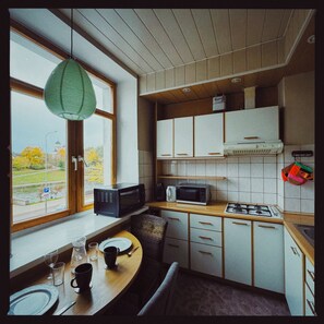 A compact kitchen with a dining area, featuring a large window, wooden cabinets, and modern appliances. - Old Town Riverside Apartment, Retro Vibe & River Panorama (Vilnius)