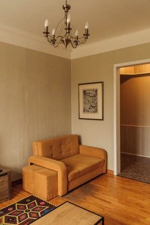 A room with a sofa, a framed picture on the wall, and a wooden floor. - Old Town Riverside Apartment, Retro Vibe & River Panorama (Vilnius)