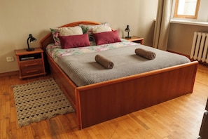 A wooden bed with a grey knitted cover, two rolled towels, and floral bedding. - Old Town Riverside Apartment, Retro Vibe & River Panorama (Vilnius)