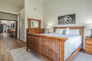 A bedroom with a wooden bed, a nightstand, a dresser, a mirror, and a wall-mounted picture. - Communal Hot Tub | Fireplace (Mammoth Lakes)