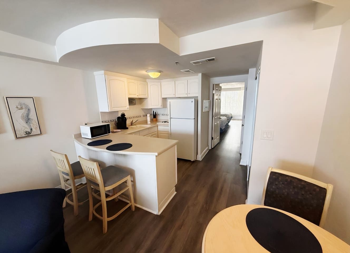 A compact kitchen with a central island, white cabinets, and a microwave. There is a dining area with a table and chairs.
