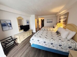 A hotel room with a bed, a desk, a television, and artwork on the walls. - Oceanfront 1 bdrm w/balcony, pool, hot tub & more (Daytona Beach)