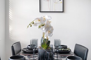 A dining table with a vase of white orchids, surrounded by black plates and clear glasses. - Modern Luxury Apartment City Centre (Birmingham)