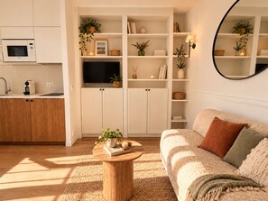 A modern living room with a sofa, a coffee table, and a kitchen area with a microwave. - New Listing (Paris)