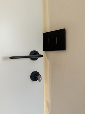 A door with a black handle and a keyhole, a black panel on the wall, and a white wall. - Apartment in the City Centre 'Vittorio Amedeo II Apartment' (Torino)