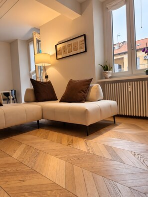 A modern living room with a sectional sofa, a floor lamp, a framed picture, and a window with a view of buildings. - Apartment in the City Centre 'Vittorio Amedeo II Apartment' (Torino)
