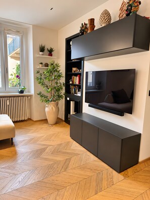 Una sala de estar moderna con televisor empotrado, una planta grande en maceta y un suelo de madera con estampado de espiga.