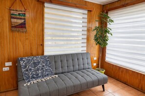 A grey sofa with a patterned throw, wooden paneled walls, and a potted plant. - New Listing (Coyhaique)