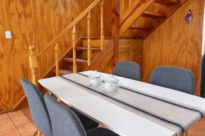 A dining area with a table set for two, wooden staircase, and a wall with a wooden panel design. - New Listing (Coyhaique)
