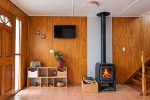 A room with a wooden interior, a television mounted on the wall, a wood-burning stove, and a staircase. - New Listing (Coyhaique)