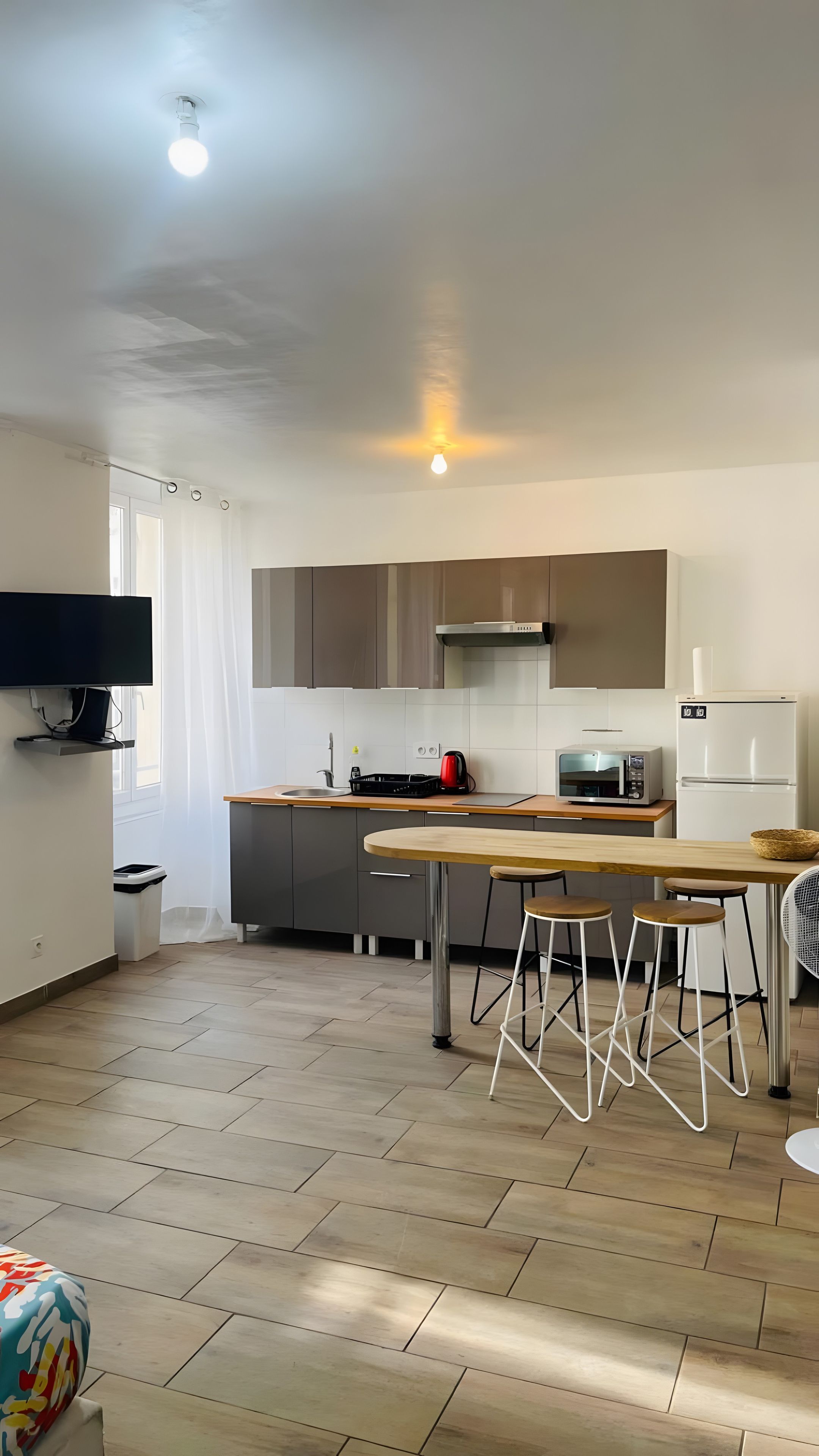 Une cuisine moderne avec un coin repas, un plancher en bois et un téléviseur à écran plat fixé au mur.