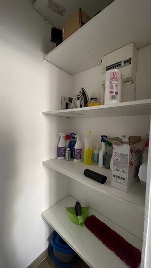 A white shelf with cleaning supplies, a yellow bottle, and a green container. - Apartment 'Studio Dans Le Centre De Marseille' with Wi-Fi and Air Conditioning (Marseille)