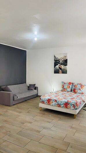 A modern bedroom with a grey sofa, a bed with a floral bedspread, and a wall-mounted picture. - Apartment 'Studio Dans Le Centre De Marseille' with Wi-Fi and Air Conditioning (Marseille)