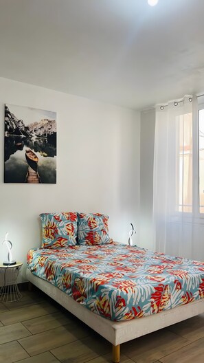 Quarto com cama, quadro pendurado na parede, mesa de cabeceira e janela com cortinas.