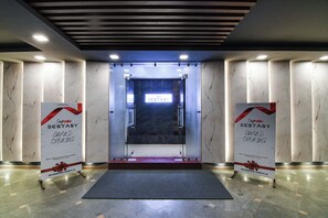 Entrada de hotel con suelo de mármol, puerta de vidrio y dos banderines a cada lado.