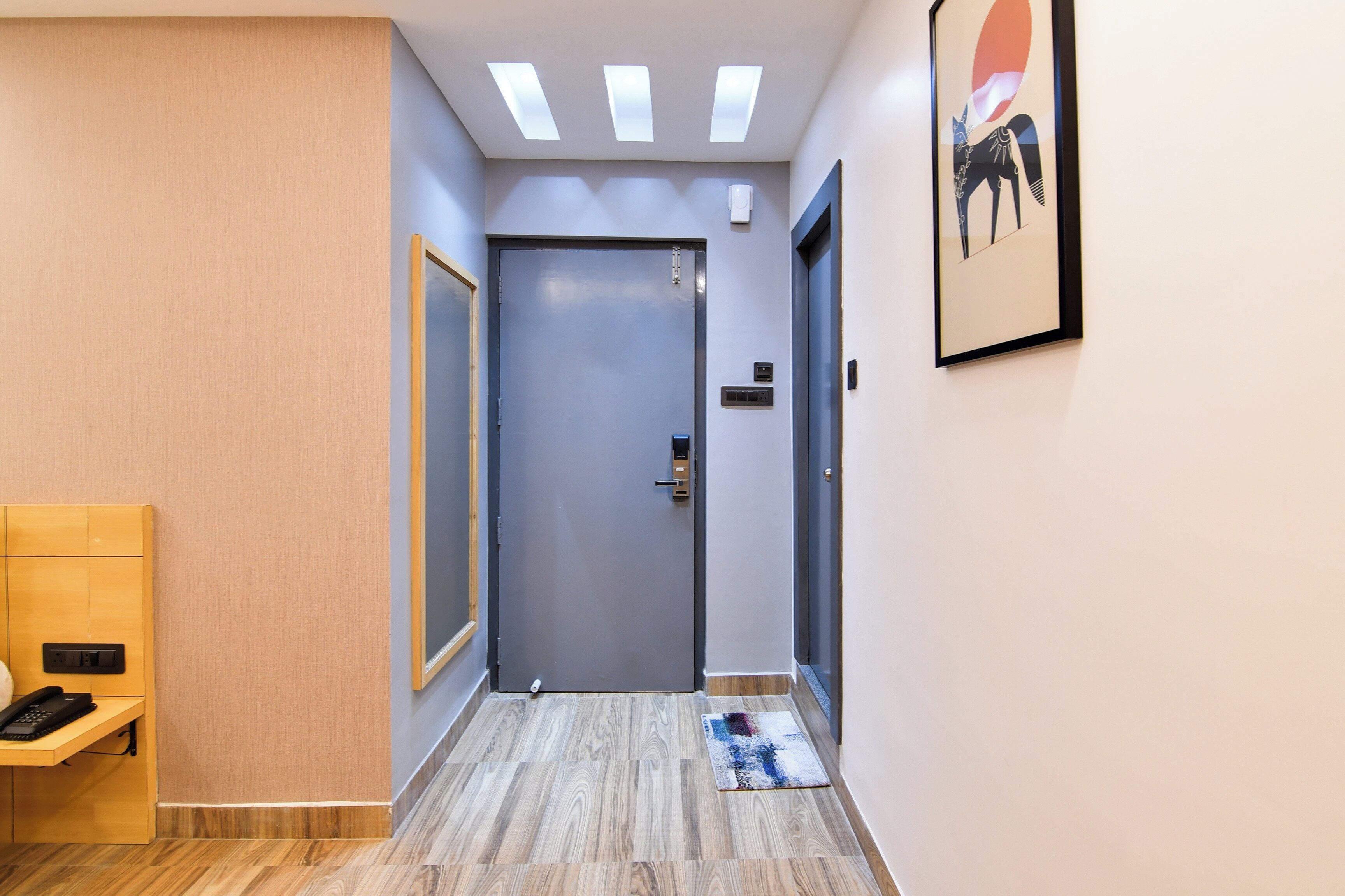 A hallway with a closed door, a telephone, and a framed artwork on the wall.