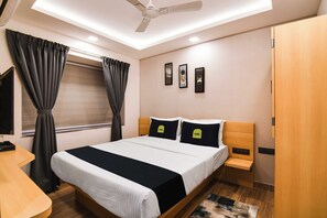 Habitación de hotel moderna con cama, mesitas de noche, escritorio, ventilador de techo y ventana con cortinas.