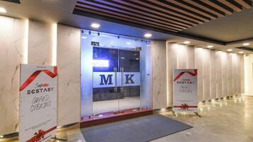 A hotel entrance with a modern design, featuring a glass door with the letters 'M K' and a sign indicating a grand opening.