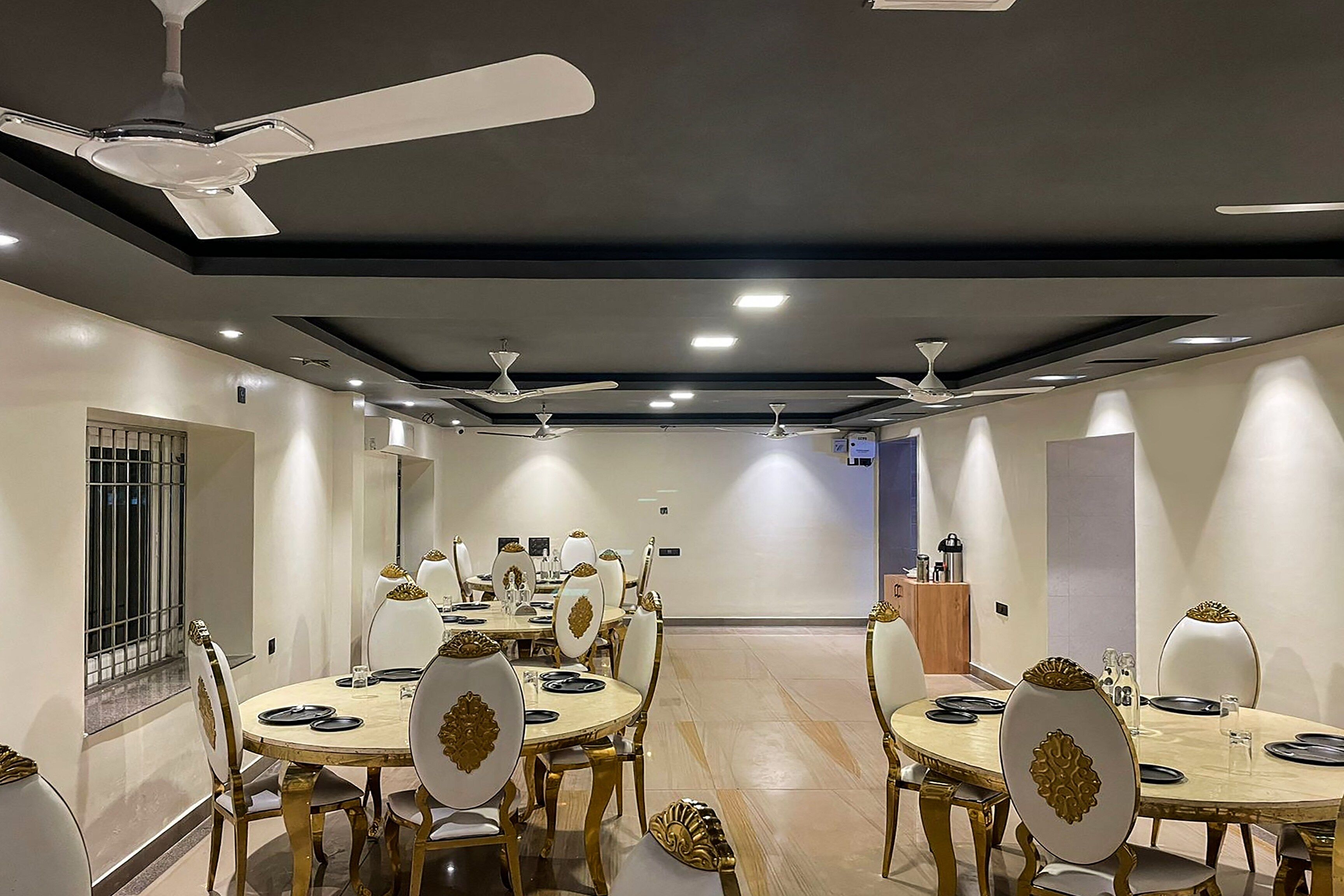 A dining area with round tables, chairs, ceiling fans, and recessed lighting.