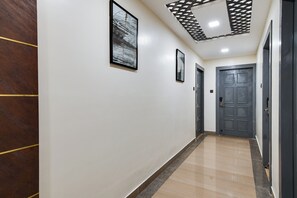Un pasillo con un panel de madera a la izquierda, suelo de baldosas y una puerta al final.