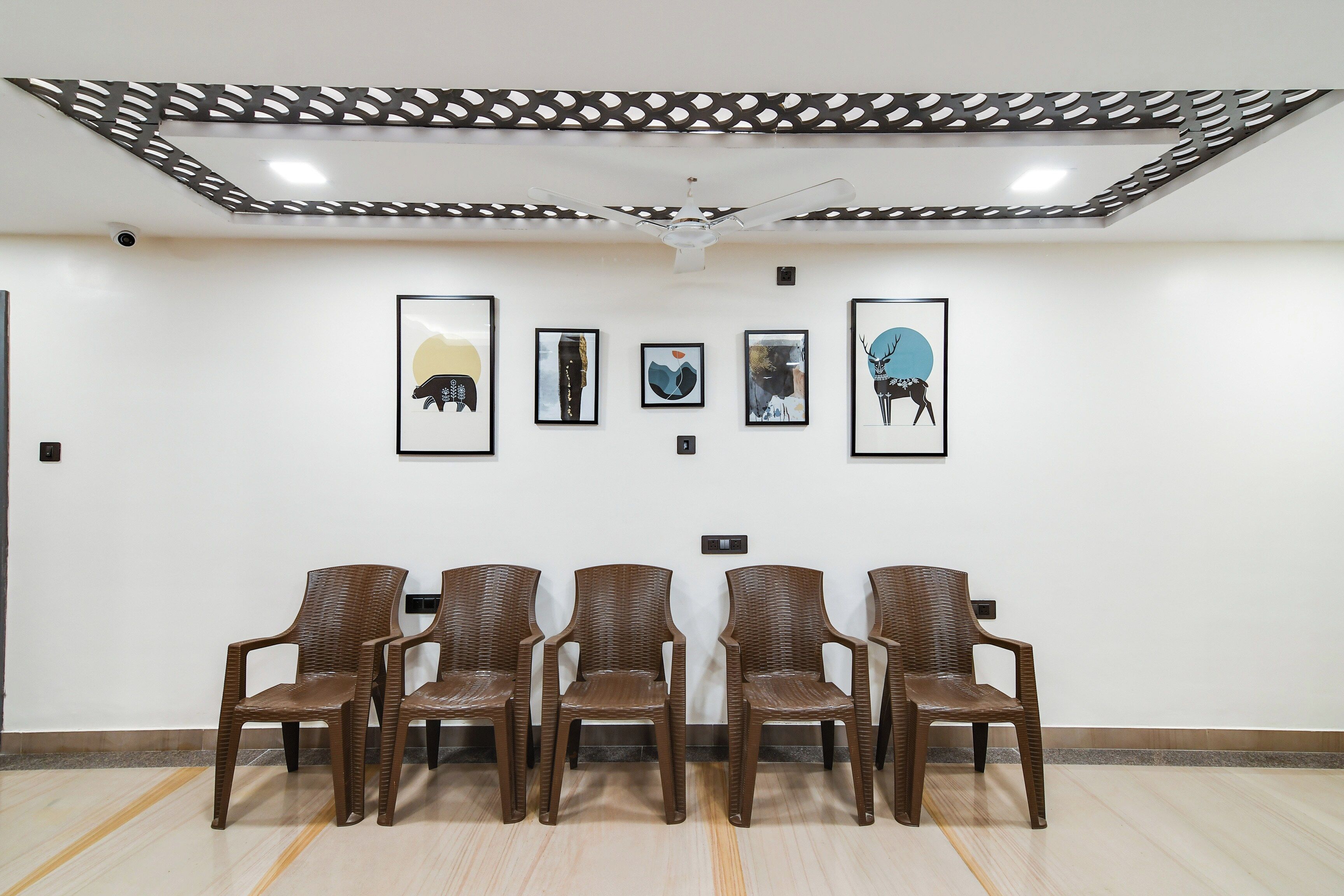 A waiting area with five brown chairs and four framed artworks on the wall.