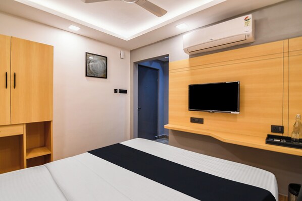 A hotel room with a bed, a television mounted on the wall, a wardrobe, and an air conditioning unit.