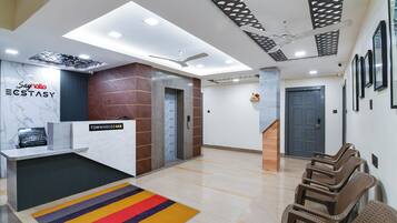 A reception area with a marble counter, a reception desk, a staircase, and a waiting area with chairs.