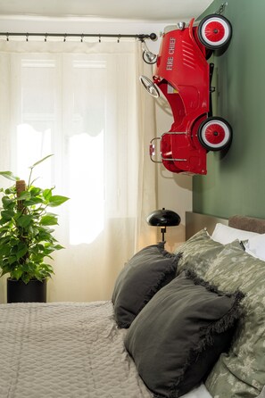 A bedroom with a bed, a potted plant, a red toy car, and a lamp. - New Listing (Modena)
