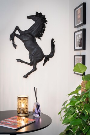 A wall-mounted sculpture of a horse, a framed photograph, a table with a magazine, a candle, and a potted plant. - New Listing (Modena)