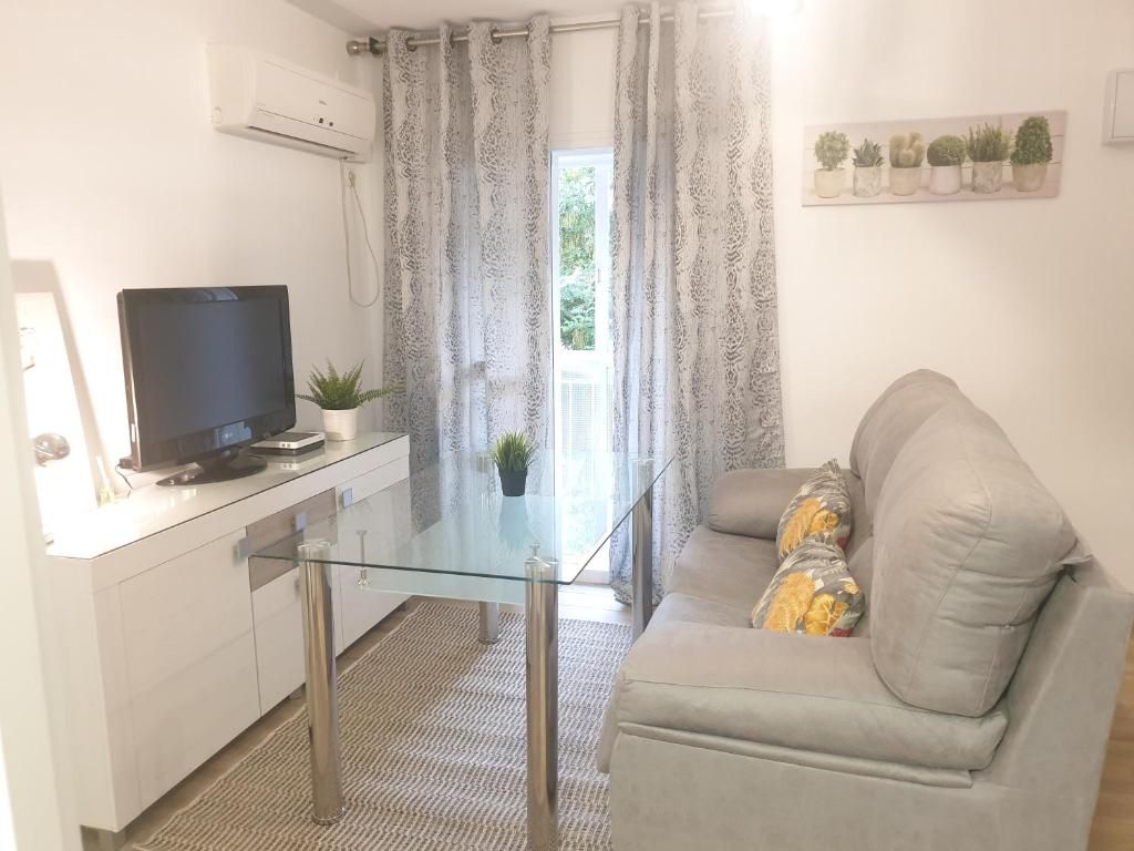 Un espace de vie moderne comprenant une table à manger avec un plateau en verre, un canapé avec des coussins, un téléviseur à écran plat et une plante en pot.