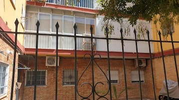 Une cour avec un bâtiment en briques, une clôture en métal noir et un pot de fleurs.