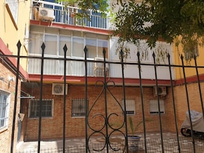 Une cour avec un bâtiment en briques, une clôture en métal noir et un pot de fleurs.