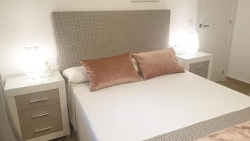 A neatly made bed with a patterned headboard, a bedside table with a lamp, and a drawer unit.