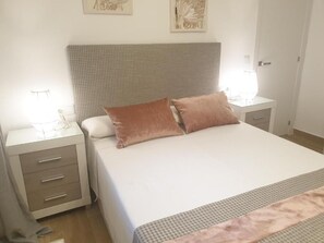 Un lit bien fait, avec une tête de lit à motifs, une table de chevet avec une lampe et une commode.