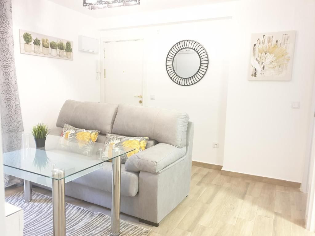 A living room with a glass coffee table, a grey sofa, and a round mirror on the wall.