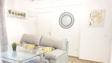 A living room with a glass coffee table, a grey sofa, and a round mirror on the wall.