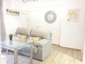 Un salon avec une table basse en verre, un canapé gris et un grand miroir rond accroché au mur.
