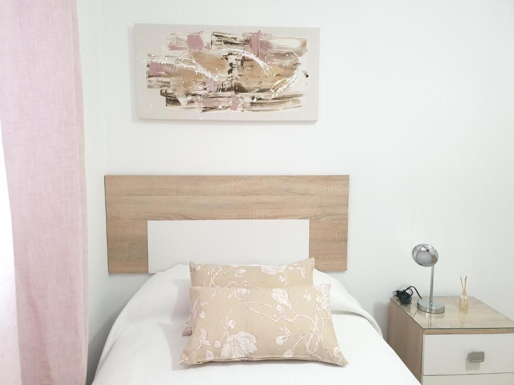 A bedroom with a wooden headboard, a bed with a floral pillow, a bedside table with a lamp, and a wall-mounted abstract painting.