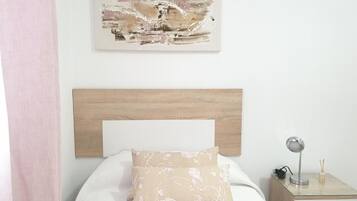 A bedroom with a wooden headboard, a bed with a floral pillow, a bedside table with a lamp, and a wall-mounted abstract painting.