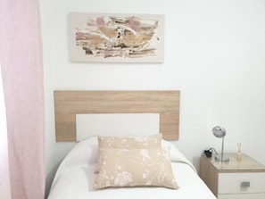 Een slaapkamer met een houten hoofdbord, een bed met een bloemenkussen, een nachtkastje met een lamp en een abstract schilderij aan de muur.