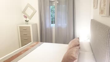 Une chambre à coucher avec un lit, une table de chevet, un miroir et une fenêtre avec des rideaux.