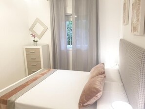 Een slaapkamer met een bed, nachtkastje, spiegel en een raam met gordijnen.