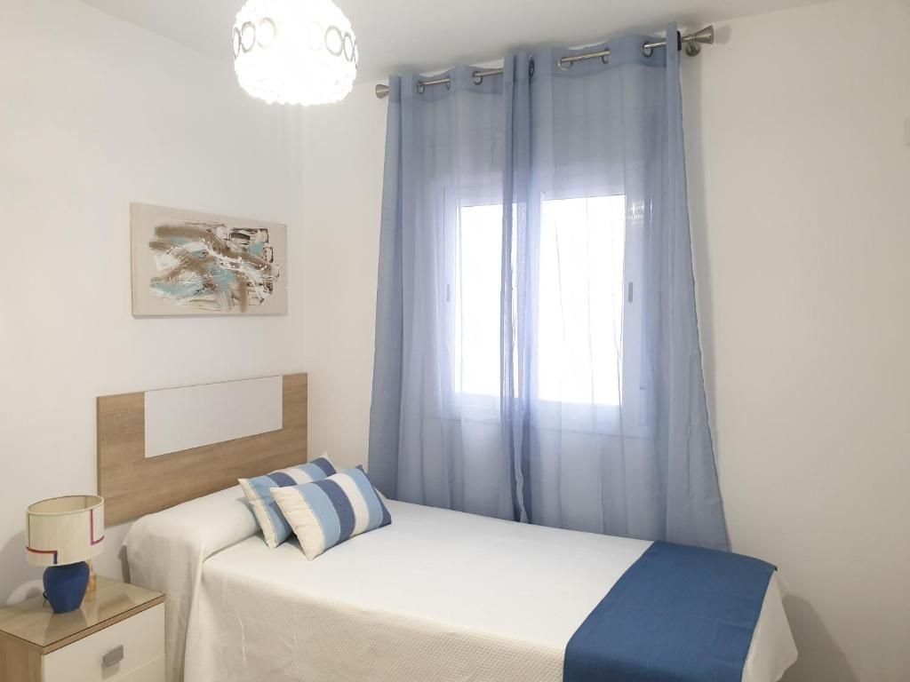 Une chambre à coucher avec un lit, une table de chevet, une lampe, un tableau et des rideaux en voile.
