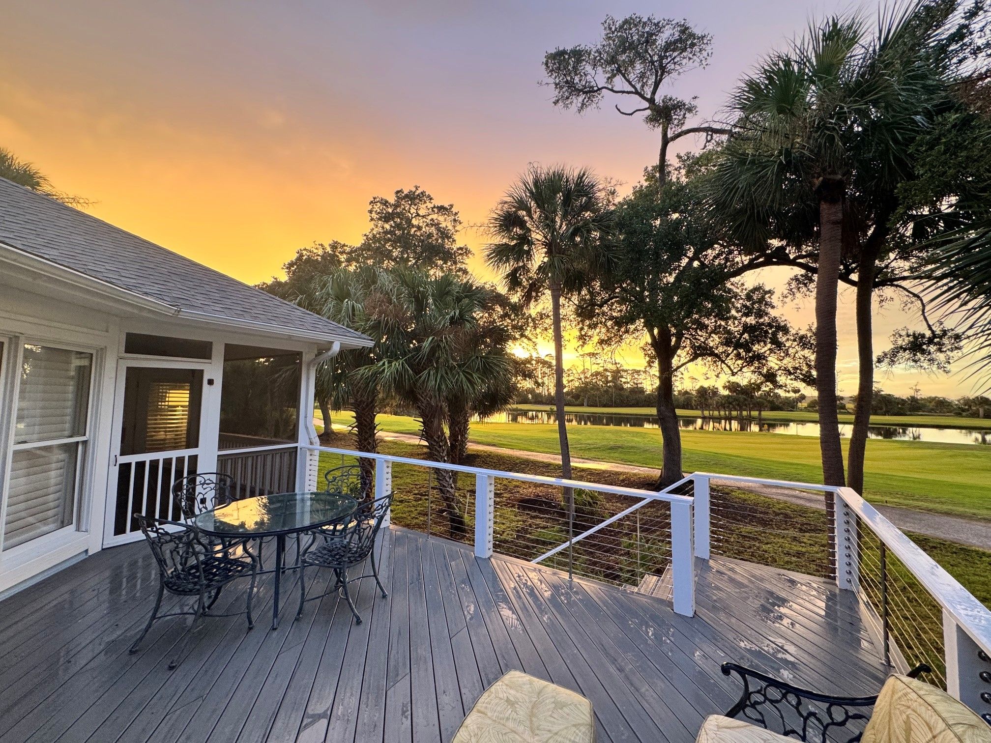 A wooden deck with outdoor furniture, overlooking a golf course and a body of water.