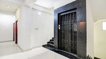 Un interior moderno con una escalera que conduce a un ascensor de tonos oscuros, paredes blancas y un piso de baldosas impecable.