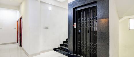 A modern interior with a staircase leading to a dark-toned elevator, white walls, and a clean tiled floor.
